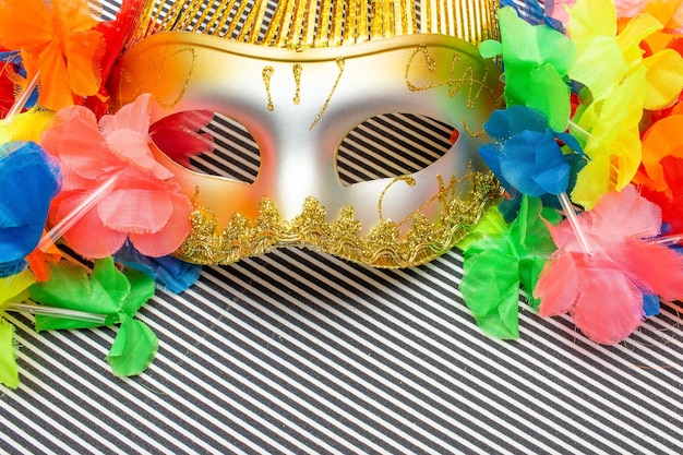 Золотая карнавальная маска на черно-белом полосатом фоне и разноцветные цветы
