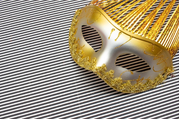 Golden carnival mask on a black and white striped background