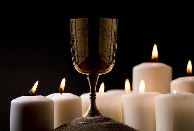 Photo golden christian chalice on ground with burning candles black background night