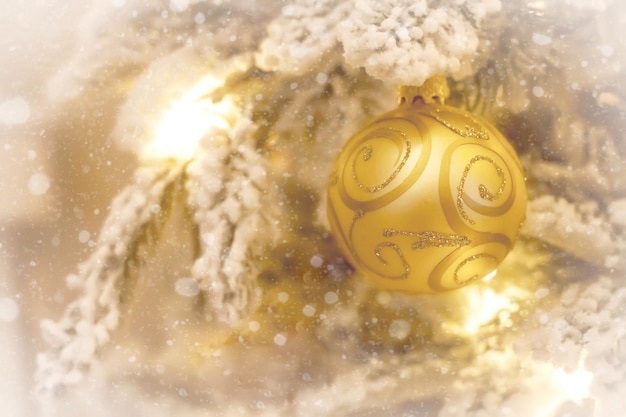 Золотой Рождественский бал на заснеженной ветке дерева. Новогодний фон с украшениями и размытыми огнями на спине. Мягкий фокус