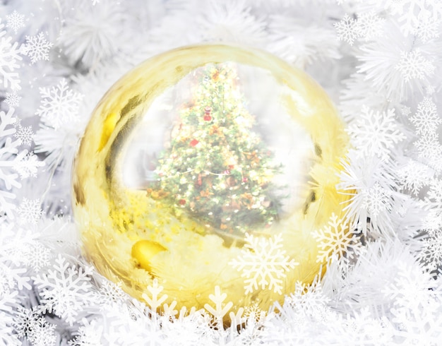 Foto sfera dorata di natale con il reticolo di riflessione e dei fiocchi di neve del pino.