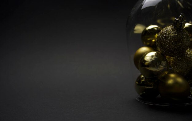 золотые елочные шары в перевернутом прозрачном бокале крупным планом на черном фоне