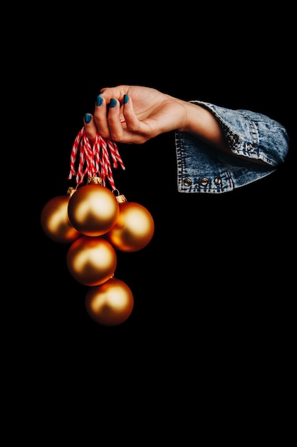 Золотые новогодние шары в руке женщины на черном фоне