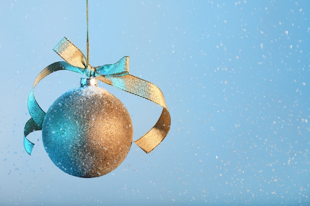 Golden christmas bauble on blue snowing