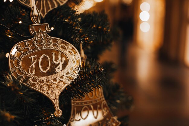 Golden Christmas toy with text Joy hanging on the tree. Golden bokeh lights on festive background
