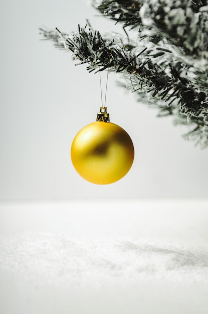 Golden Christmas tree toy ball on artificial fir tree with snow on white . 