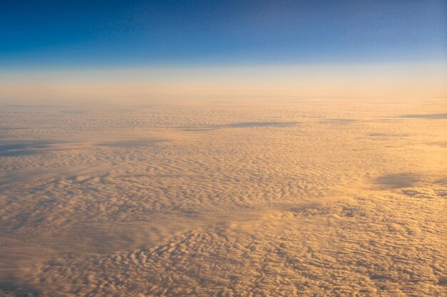 青い空の上の金色の雲日の出時の飛行機の側面の窓からの眺めの上の外側、