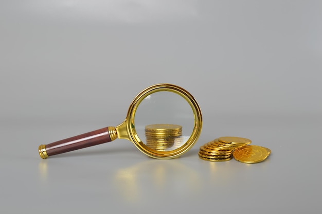 Magnifying glass with gold and silver coins on white background