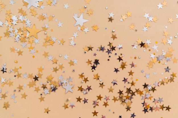 Golden confetti stars on beige background top view