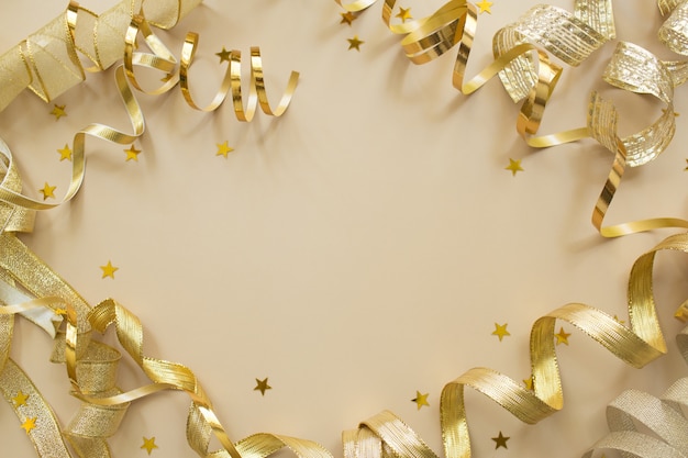 Golden confetti, tapes on beige background. Christmas composition. Festive holiday backdrop.