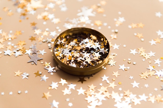 Golden confetti in tin jar on beige background