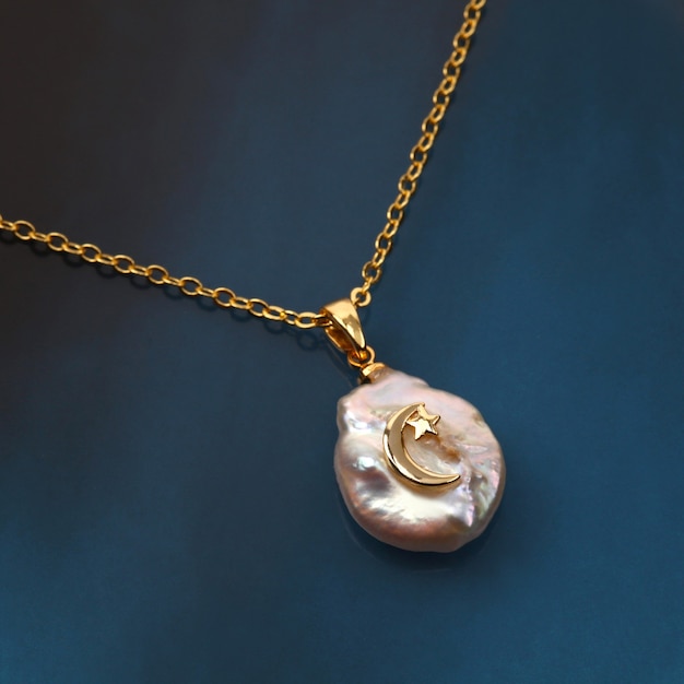 Golden crescent moon baroque pearl pendant with gold chain on black blue gradient background