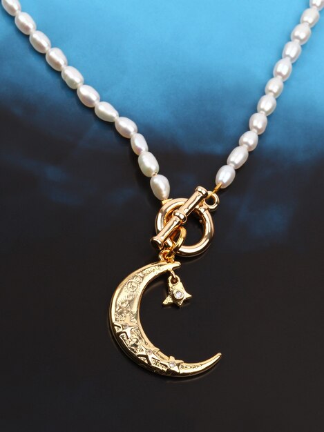 Golden crescent moon pendant with pearl necklace on black blue gradient background