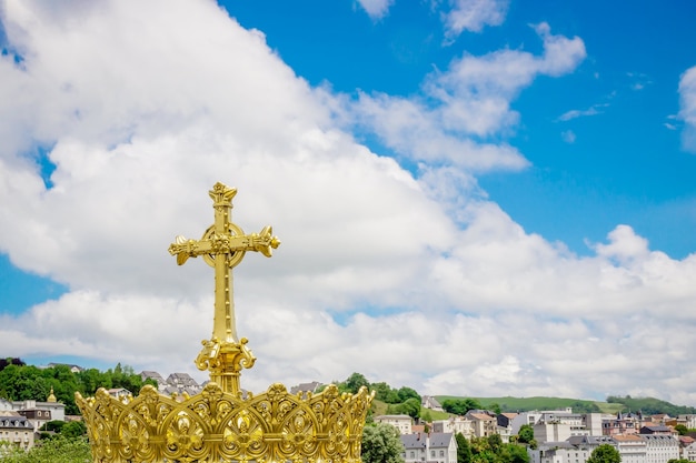 Golden cross and crown on the blue sky background in Lourdes France