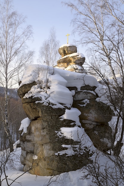 ツェルコフカ山の雪の自然彫刻で覆われた巨大な石の岩の上の黄金の十字架