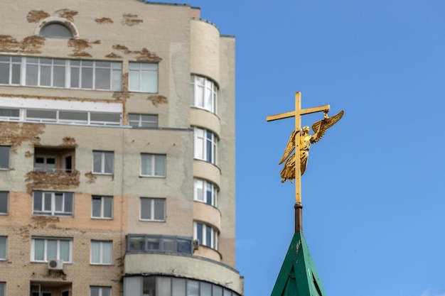 Croce d'oro con un angelo contro il cielo blu e la facciata di un condominio