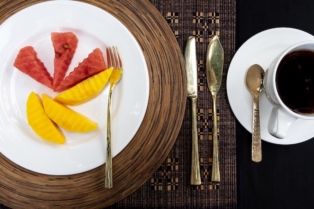 Golden cutlery laid on a table with a plate melon and a cup