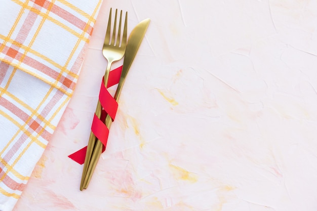 Golden cutlery in red ribbon and kitchen towel on a pink
