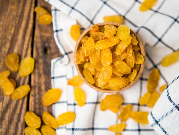 Golden dried raisins in a wooden bowl and spoon on an old wooden table