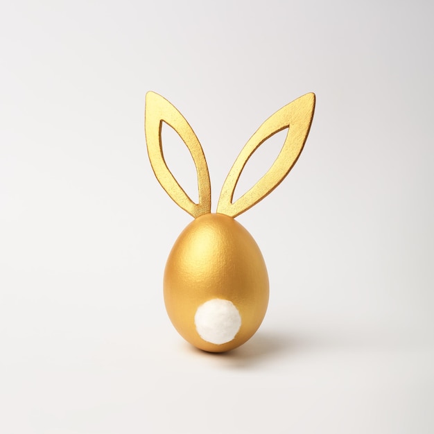 Golden Easter egg with bunny ears on white background in minimal style