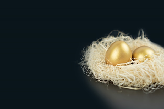 Golden eggs with straw on black background.