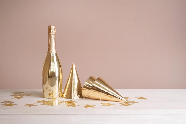 Photo golden festive caps and a bottle of champagne on the table beige festive background with copy space