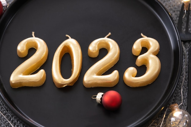 Foto figure d'oro 2023 da candele su un piatto nero su un tavolo festivo con una festa interna loftstyle di capodanno che serve un coltello forchetta tovagliolo di vimini