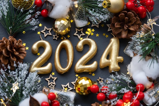 The golden figures 2024 made of candles on a black stone slate background are decorated with a festive decor of stars sequins fir branches balls and garlands Greeting card happy New Year
