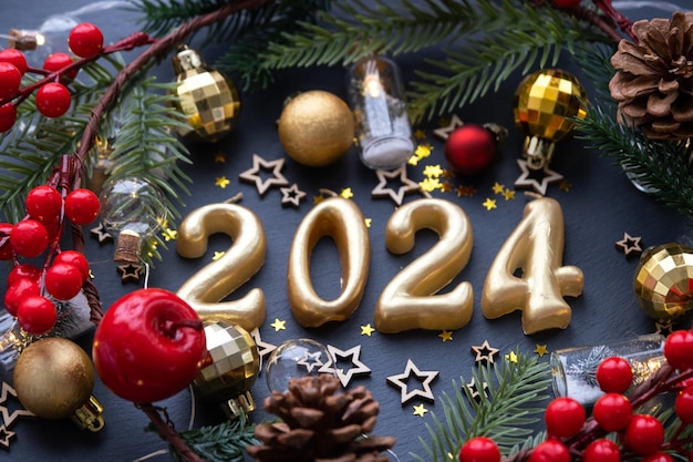 The golden figures 2024 made of candles on a black stone slate background are decorated with a festive decor of stars sequins fir branches balls and garlands Greeting card happy New Year