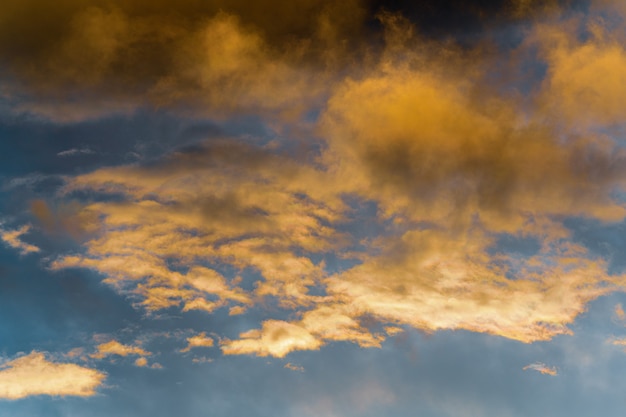 Soffici nuvole dorate illuminate da raggi che scompaiono al tramonto e nuvole temporalesche scure cielo blu