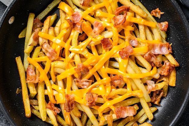 Golden French fries fried with cheddar cheese and bacon in a pan