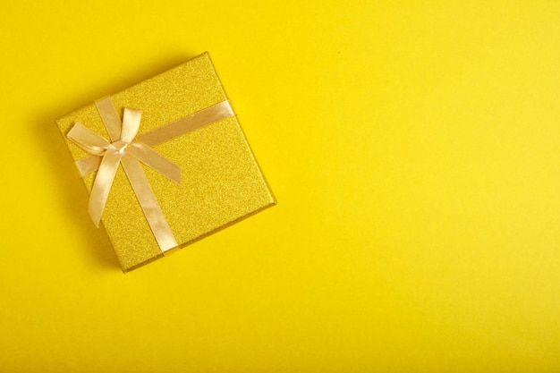 Golden gift box is tied with ribbon with bow yellow background