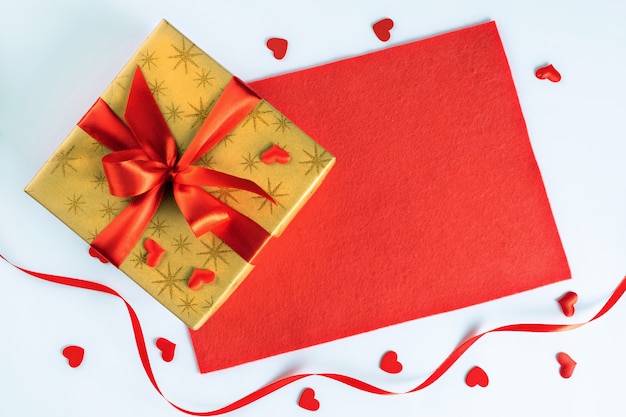 Golden gift box with red ribbon on fabric and little hearts for valentines day