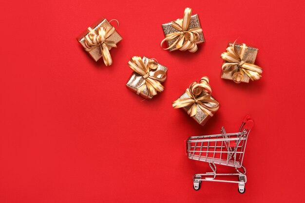 Golden gifts boxes and shopping cart on red background. Black friday sale and shopping day concept.