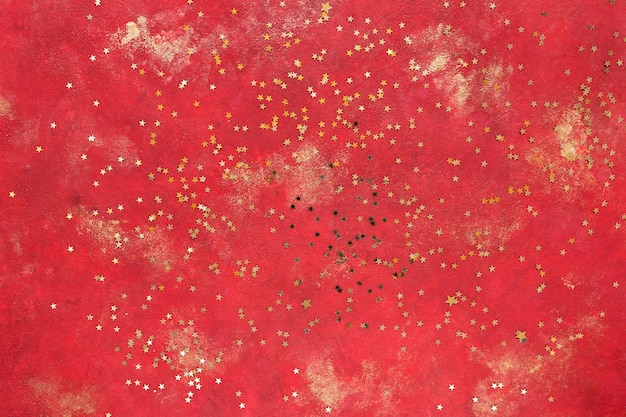 Golden glitter star shaped confetti on red and golden background. Top view, close up