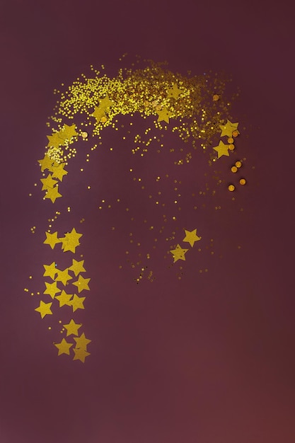 Golden glitter stars and golden sequins on a brown dark background Dreamlike glitter on the background top view Art glitter background