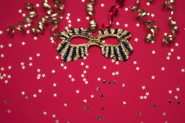 Golden glittering mask and serpentine with golden stars on red.