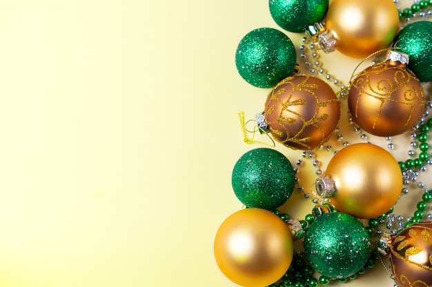 Golden and green christmas balls and decorations on yellow background with copy space