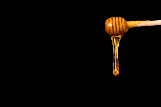 Golden honey drips from the spoon on a black background.