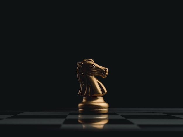 The golden horse, knight chess piece standing alone on chessboard on dark background. Leadership, influencer, strong, commander, competition, and business strategy concept.