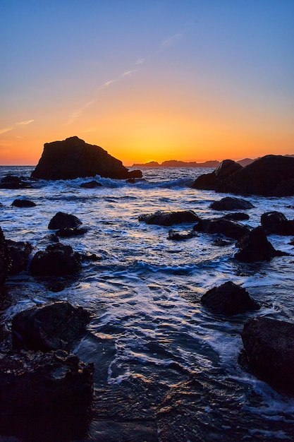 Golden hour after sunset on beach with waves around rocks