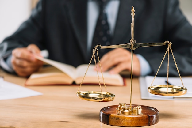 Photo golden justice scale in front of lawyer reading book on table