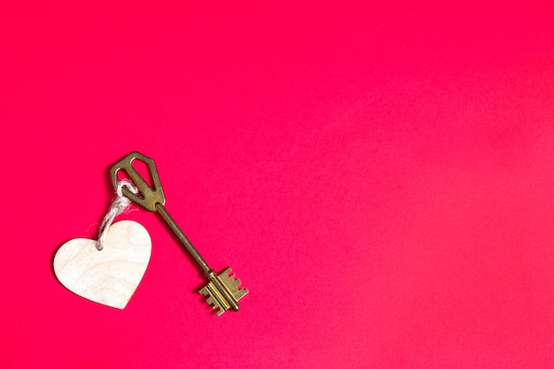 Golden key with wooden tag in the shape of a heart on a red background