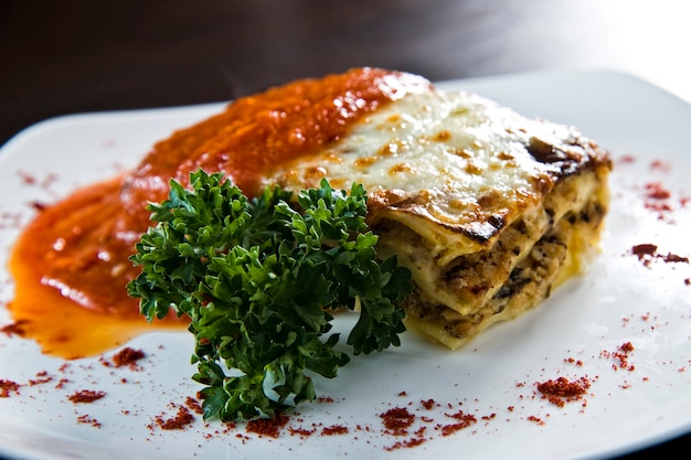 Golden lasagne with meat, tomatoes, cheese sauce and pasta in alternating layers on a wooden board garnished with basil