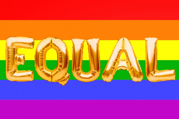 Golden letters made from balloons forming word EQUAL on pride rainbow flag background