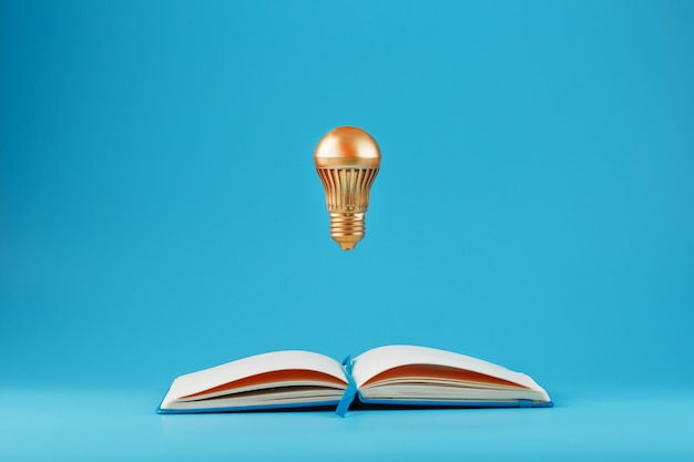 Photo a golden light bulb in levitation from an open notebook on blue.