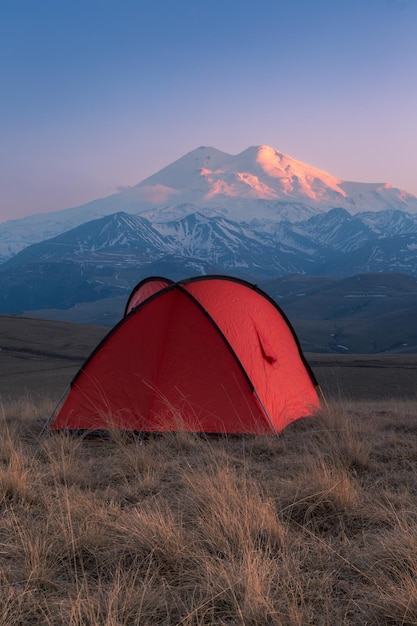 Golden light sunset with bright red tent in front of snowcovered Mount Elbrus Caucasus Russia