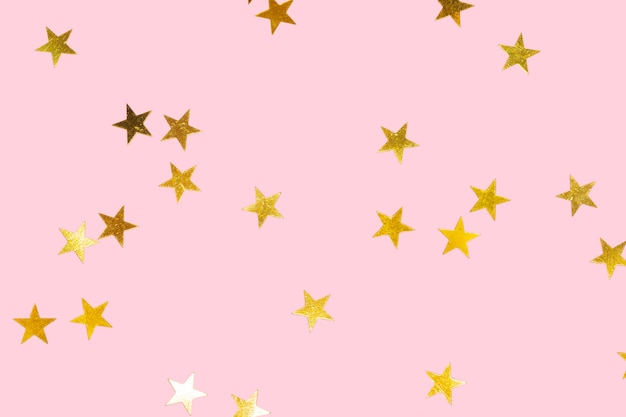 Golden metallic star confetti on a pastel pink background for christmas backdrop