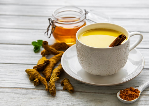 Golden milk with cinnamon, turmeric, ginger  and honey over white wooden surface