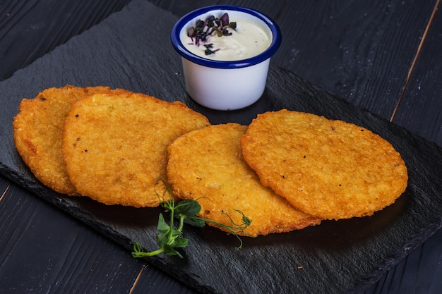 Golden pancakes on a black tray with garlic sauce